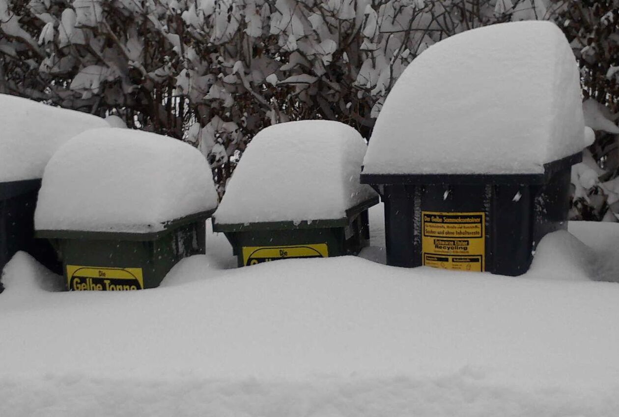 Vier bis zum oberen Drittel eingeschneite Abfalltonnen, auf den Deckeln große Schneehauben